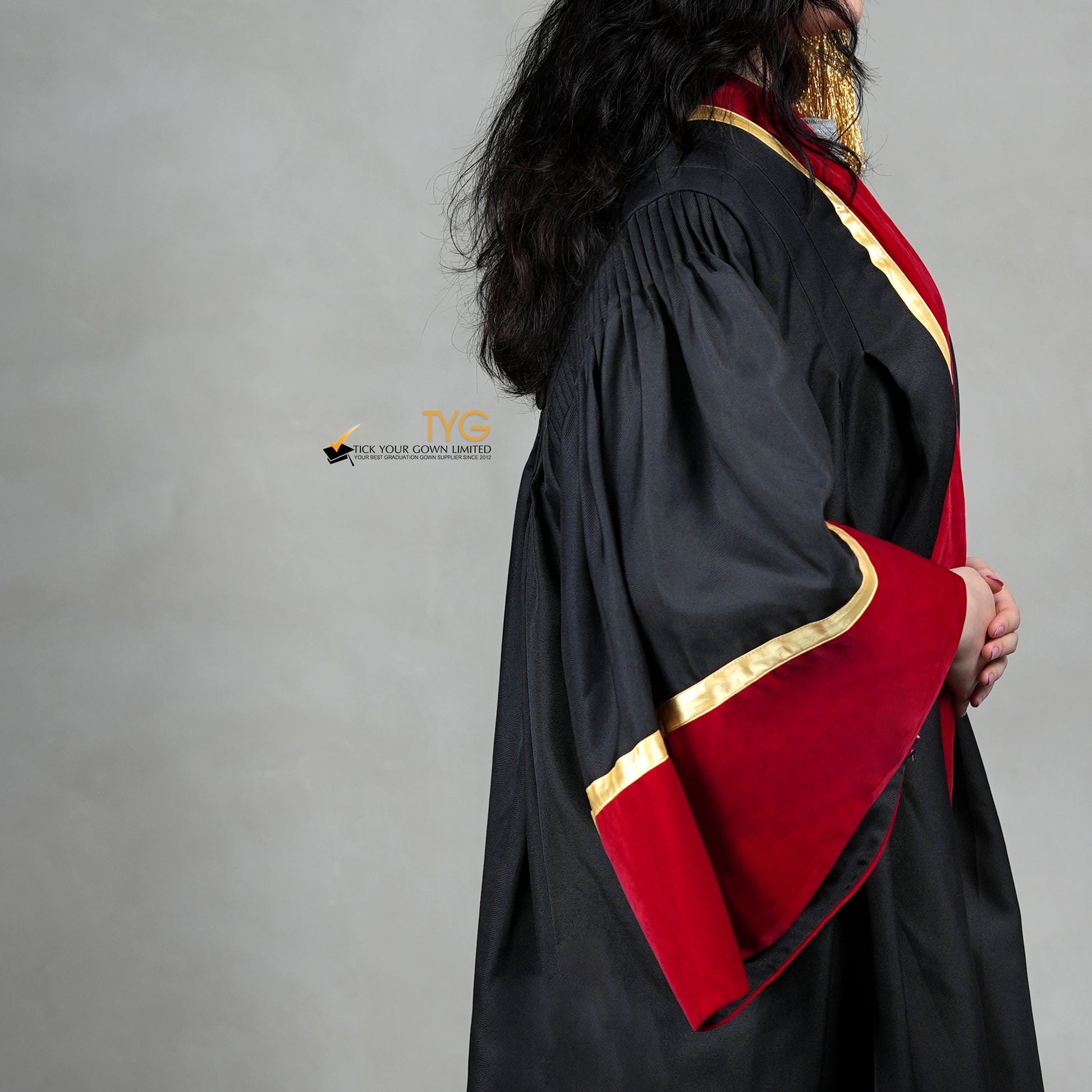 Detailed profile view of a doctoral graduation gown in black with red velvet sleeve cuffs, gold trim, and gathered shoulder pleats