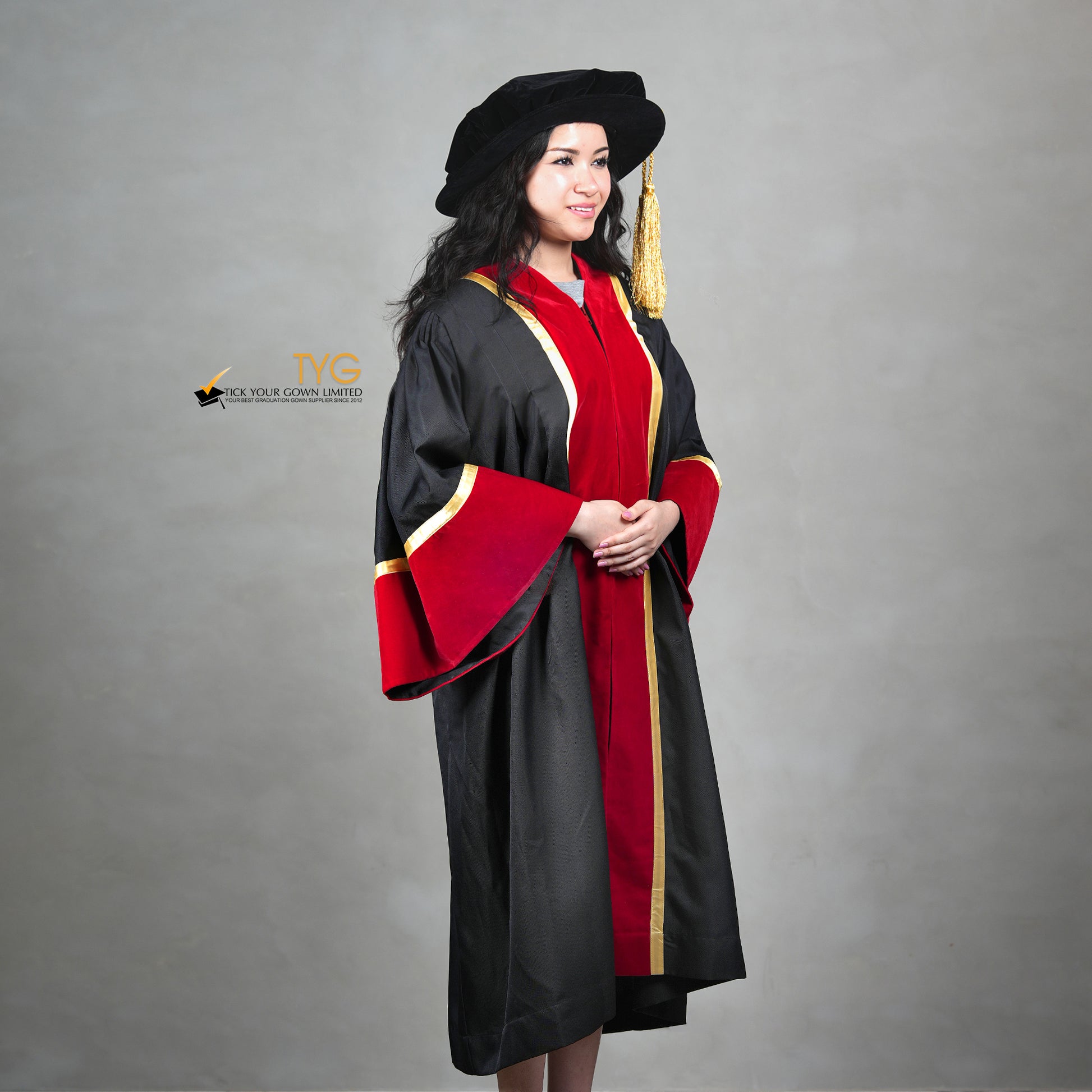 Profile view of a honorary gown in black with red velvet panels, gold trim, red velvet sleeve cuffs, and a matching doctoral bonnet with gold tassel