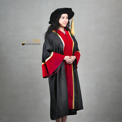 Profile view of a honorary gown in black with red velvet panels, gold trim, red velvet sleeve cuffs, and a matching doctoral bonnet with gold tassel