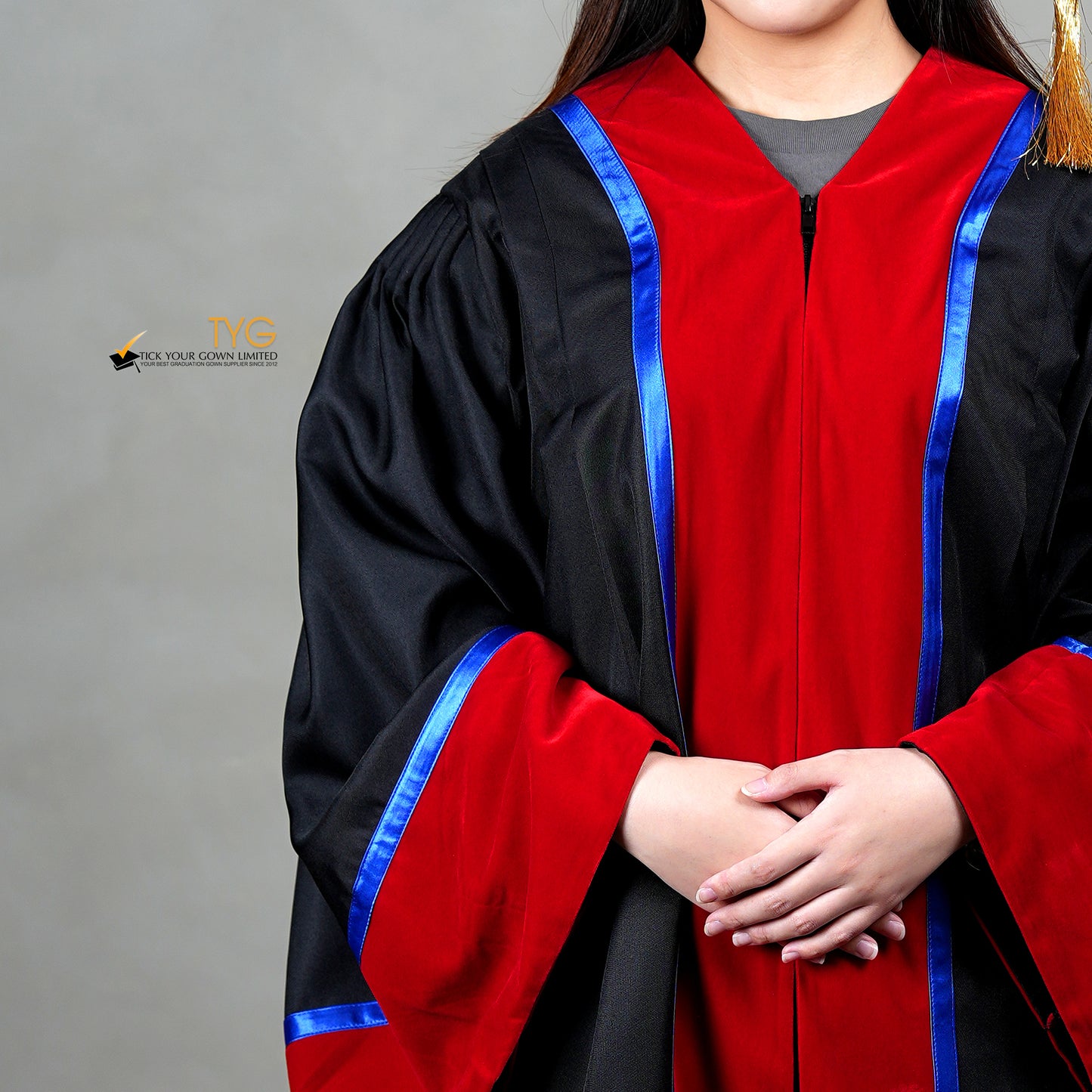 A detailed front view of a person wearing a premium honorary graduation gown in black with red velvet panels, royal blue trim and red velvet sleeve cuffs.