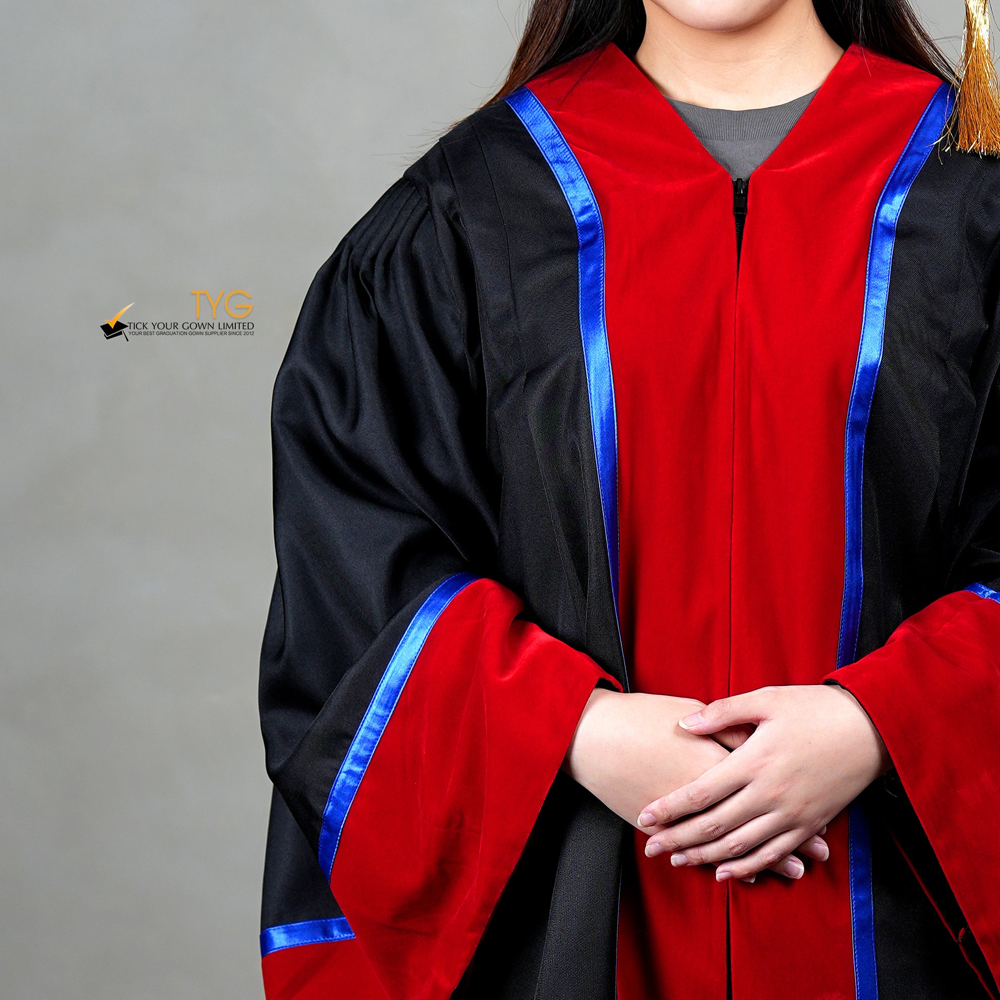 A detailed front view of a person wearing a premium honorary graduation gown in black with red velvet panels, royal blue trim and red velvet sleeve cuffs.