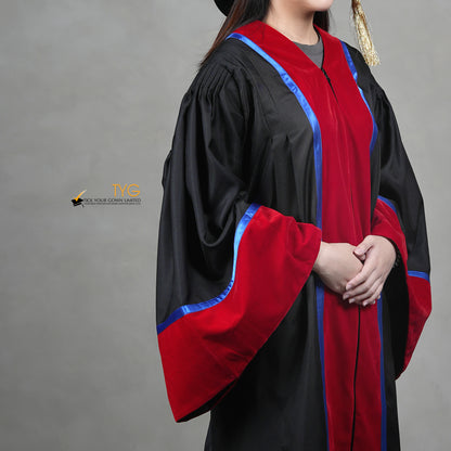 A detailed profile view of a person wearing a premium honorary graduation gown in black with red velvet panels, royal blue trim, red velvet sleeve cuffs, and a matching doctoral bonnet with gold tassel.