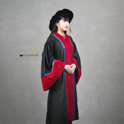 A profile view of a person wearing a premium honorary graduation gown in black with red velvet panels, royal blue trim, red velvet sleeve cuffs, and a matching doctoral bonnet with gold tassel.