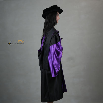 A side view of a person wearing a graduation gown in black with purple satin panels, matching purple satin sleeve cuffs, and a black doctoral bonnet with gold tassel.