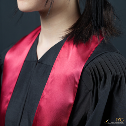 Person wearing a black graduation gown with a red graduation sash stole on a dark background